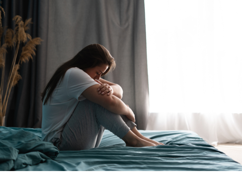 A woman sitting on a bed in a contemplative pose, symbolizing emotional recovery and healing trauma through self-reflection and inner strength.